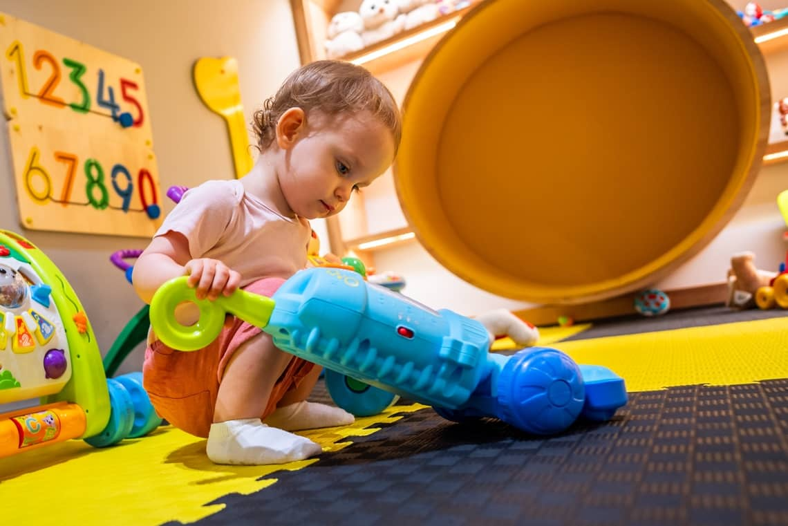 Toddler playing with a toy vacuum cleaner at 3Rs Kids Academy in Helena, Montana.